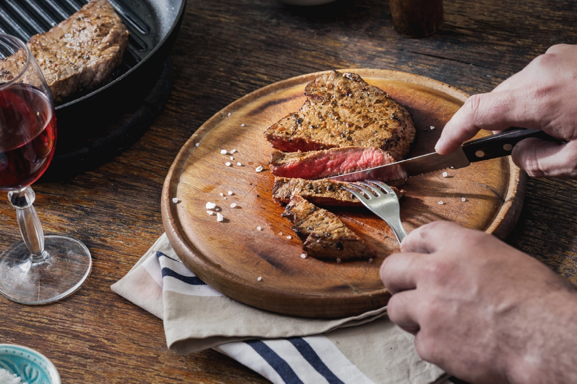 Man eating grilled steak at a wooden table
